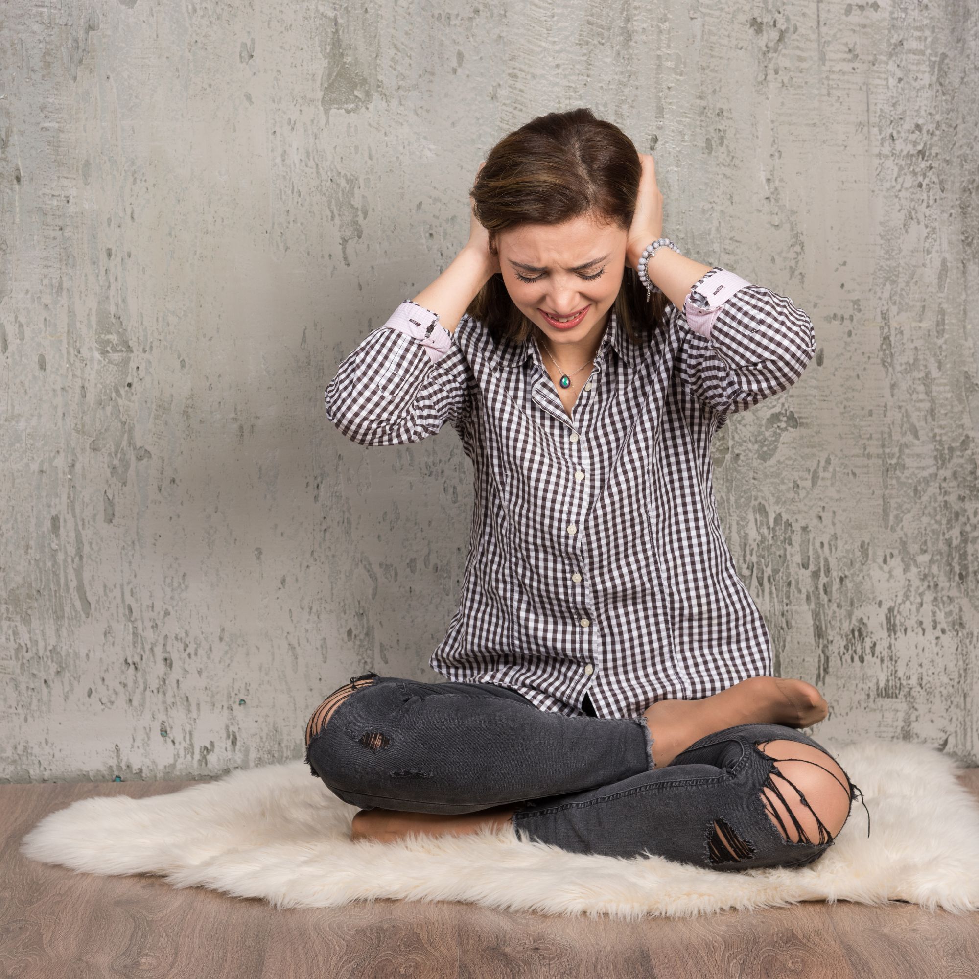 Woman sitting on floor covering her ears, showing visible discomfort due to bad acoustics and noise in a concrete room.
