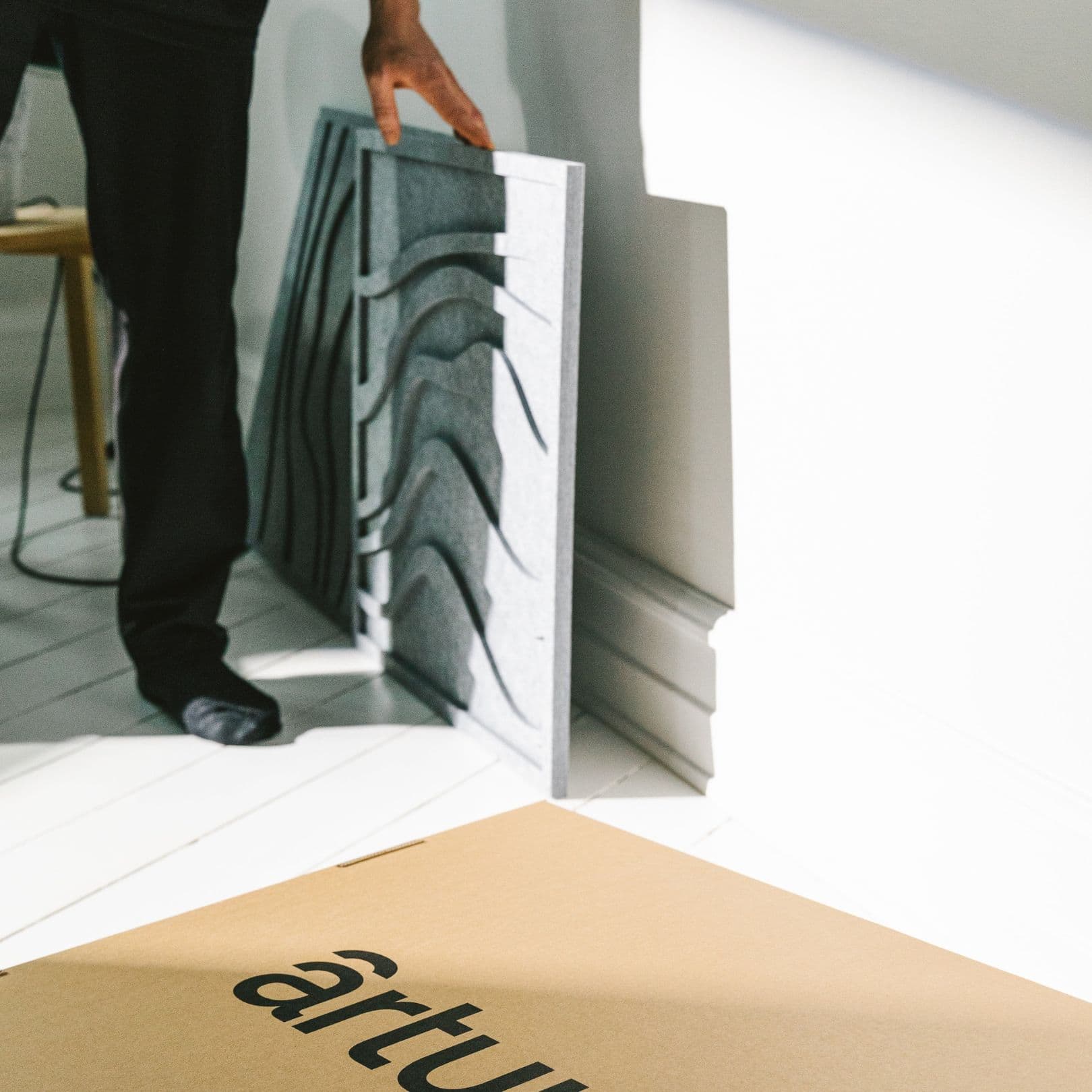 Person unpacking gray acoustic wave panels from Arturel, preparing for installation in a modern interior.